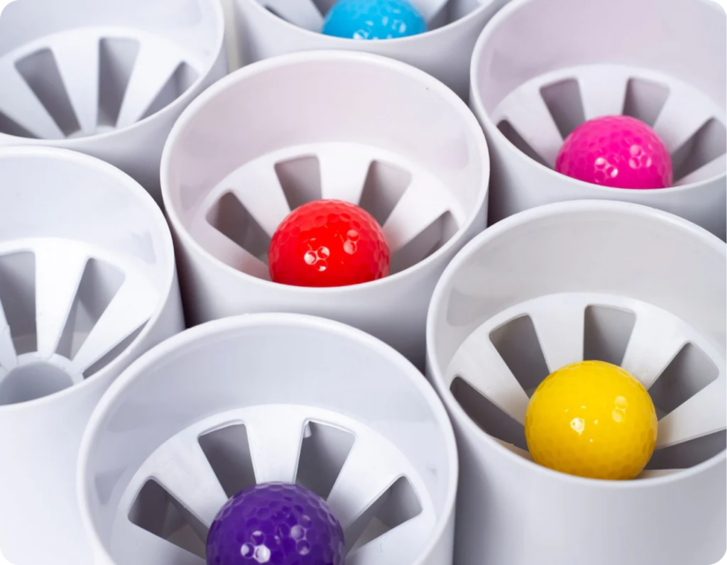 multiple mini golf putting cups with a ball in each putting cup in colours purple, red, yellow, blue and pink.